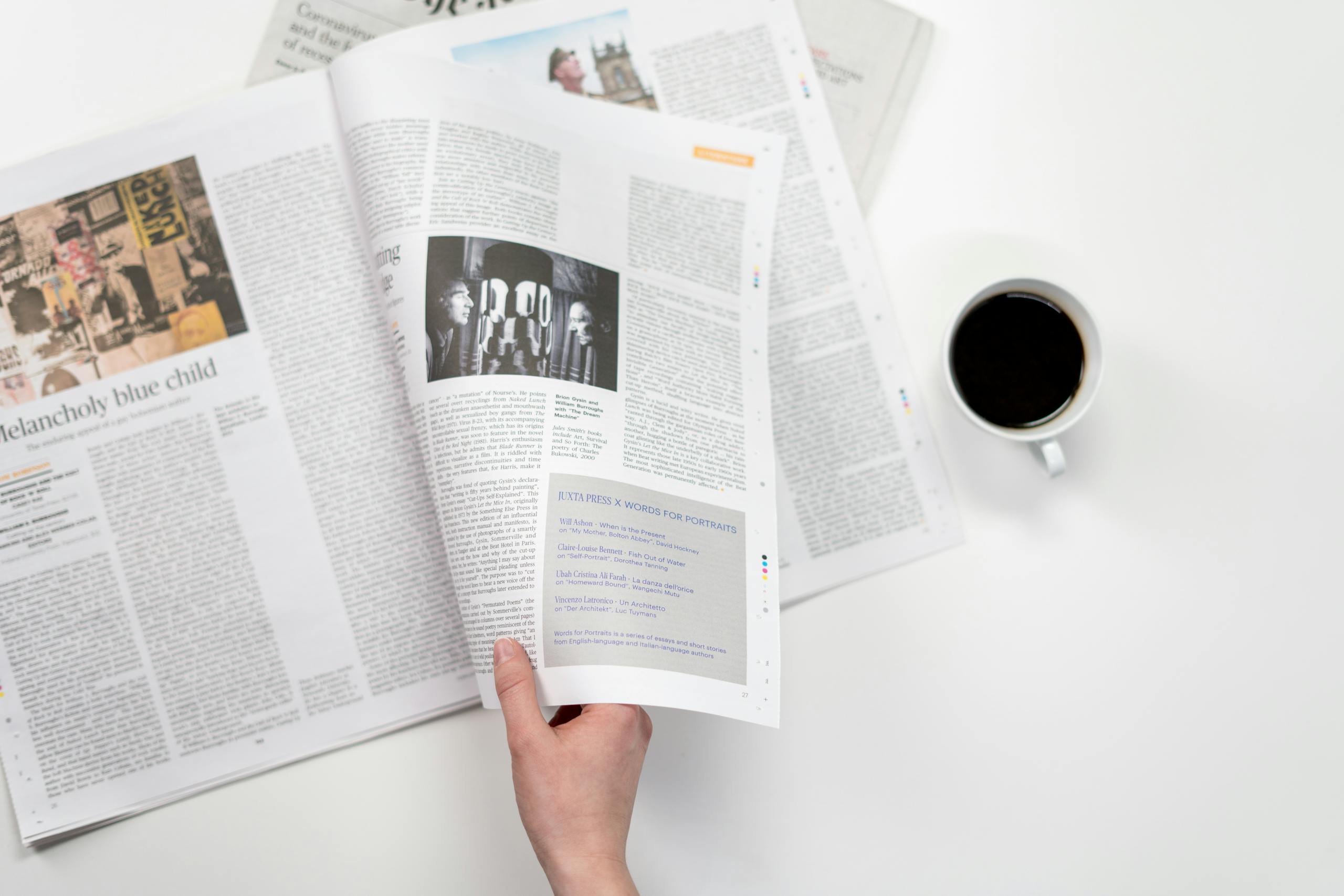 A close-up shot of a hand holding a newspaper with a coffee cup on a white surface.